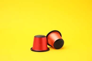 Two plastic coffee capsules on yellow background