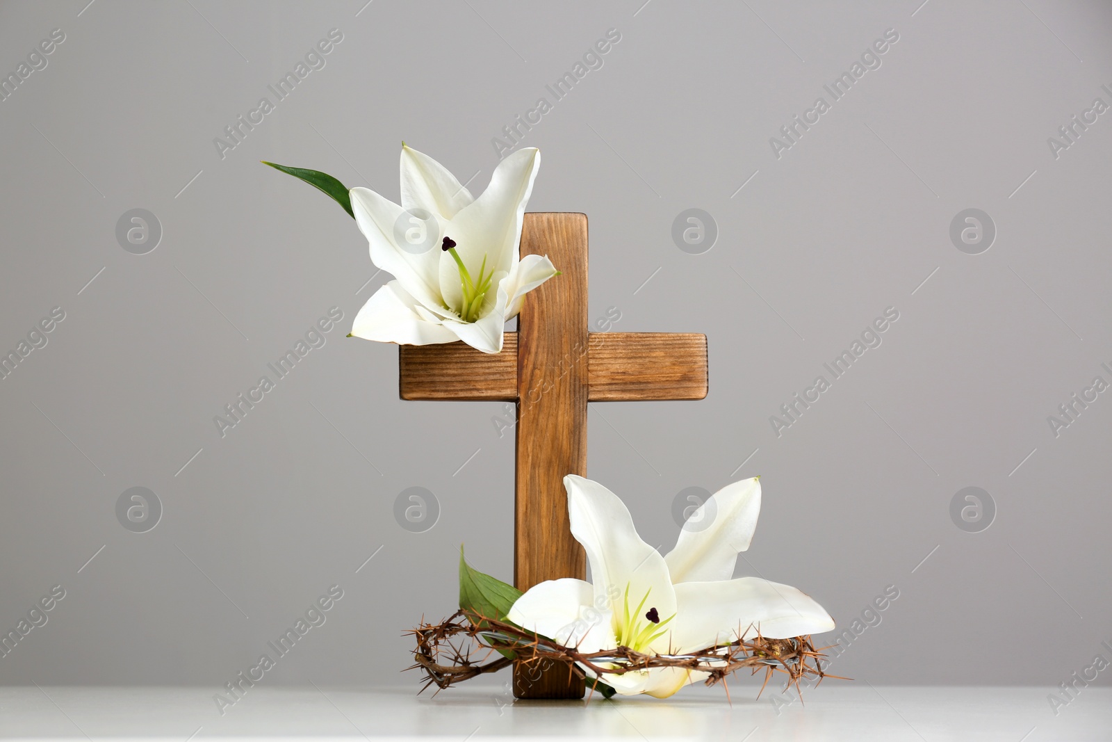 Photo of Wooden cross, crown of thorns and blossom lilies on table against color background