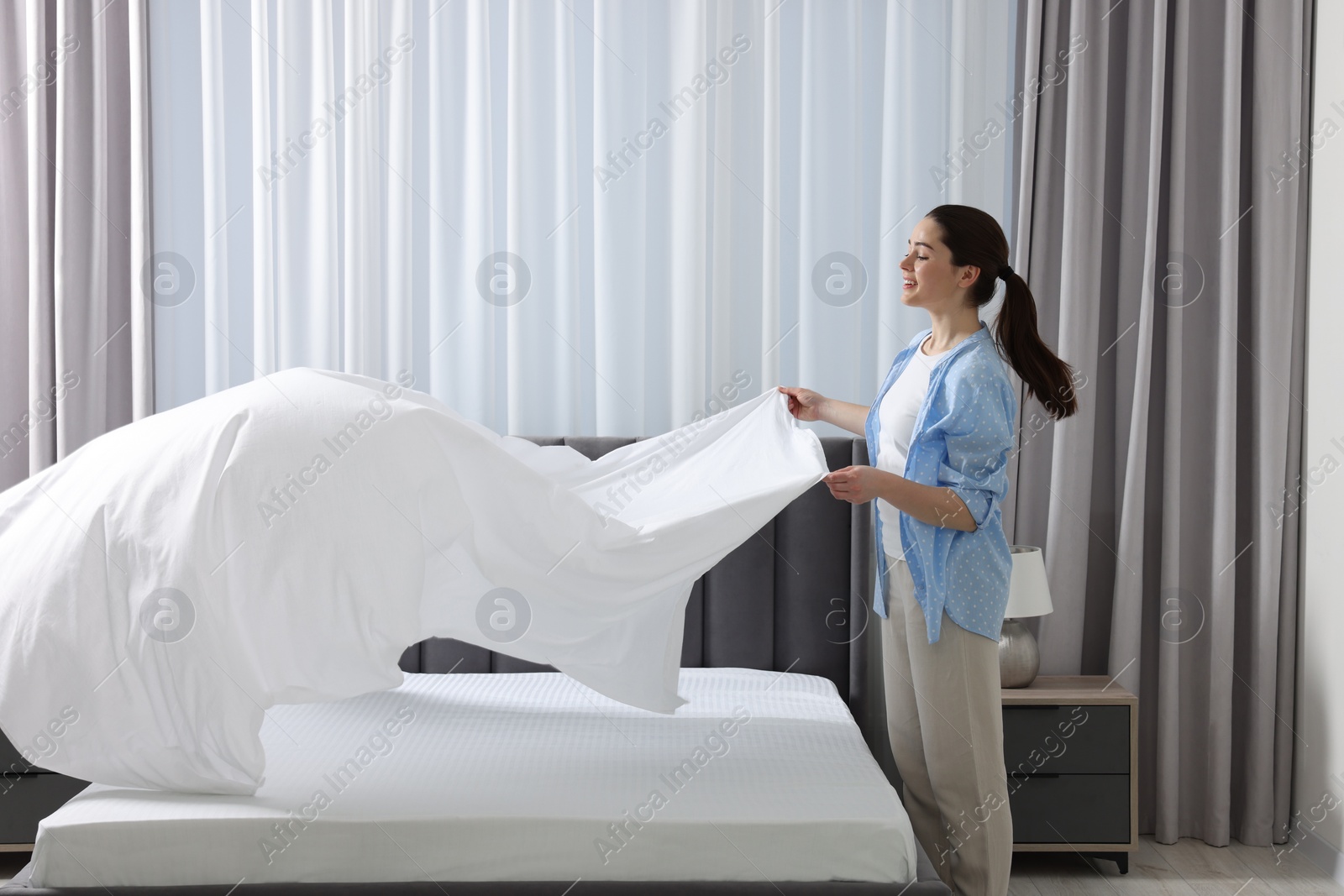 Photo of Young woman changing bed linens at home