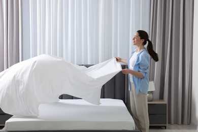 Photo of Young woman changing bed linens at home