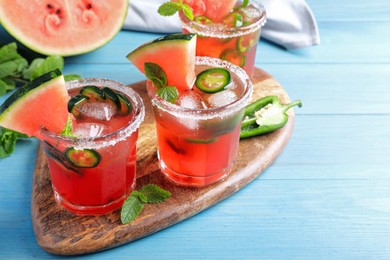 Photo of Glasses of spicy cocktail with jalapeno and mint on light blue wooden table. Space for text