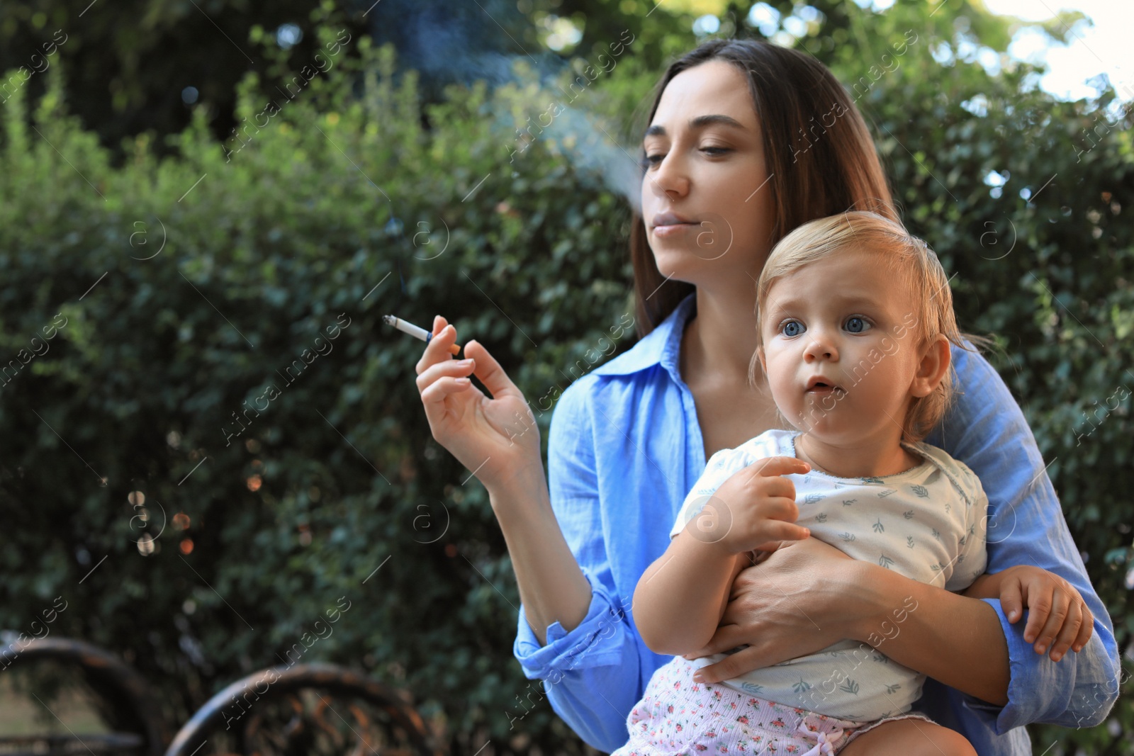 Photo of Mother with cigarette and child outdoors. Don't smoke near kids