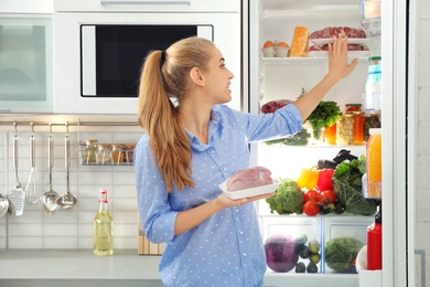 Woman taking fresh meat out of refrigerator in kitchen