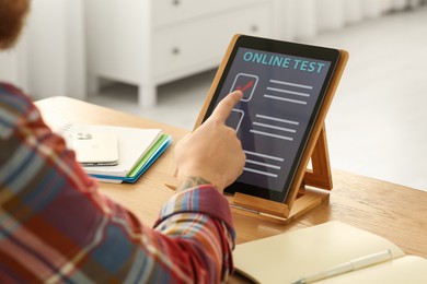 Man taking online test on tablet at desk indoors, closeup