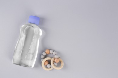 Photo of Bottle with baby oil and rattle on light grey background, flat lay. Space for text