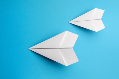 Handmade white paper planes on light blue background, flat lay