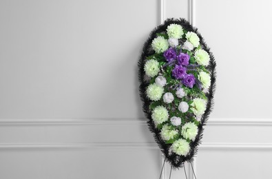 Photo of Funeral wreath of plastic flowers near white wall, space for text
