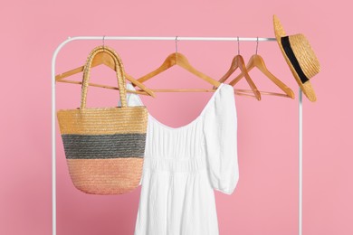 Rack with accessories and stylish white dress on wooden hangers against pink background