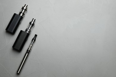 Photo of Different electronic cigarettes on grey table, flat lay with space for text. Smoking alternative