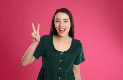 Woman showing number two with her hand on pink background