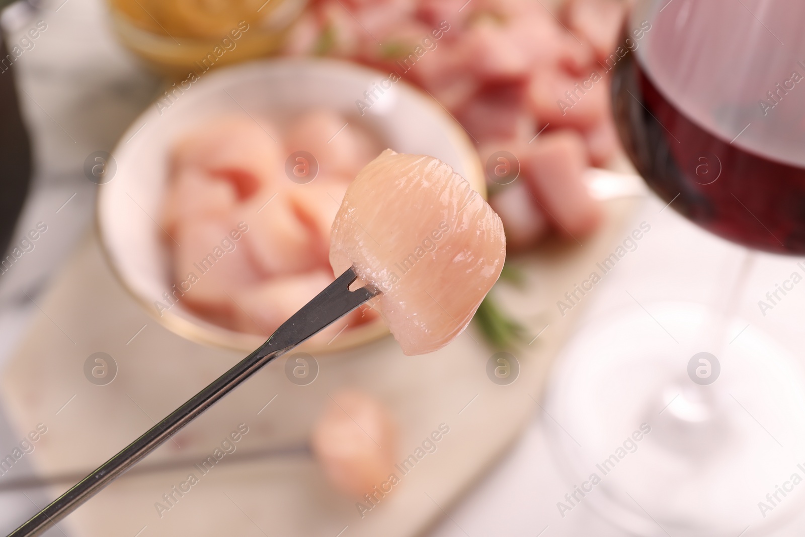 Photo of Fondue fork with raw piece of meat on blurred background