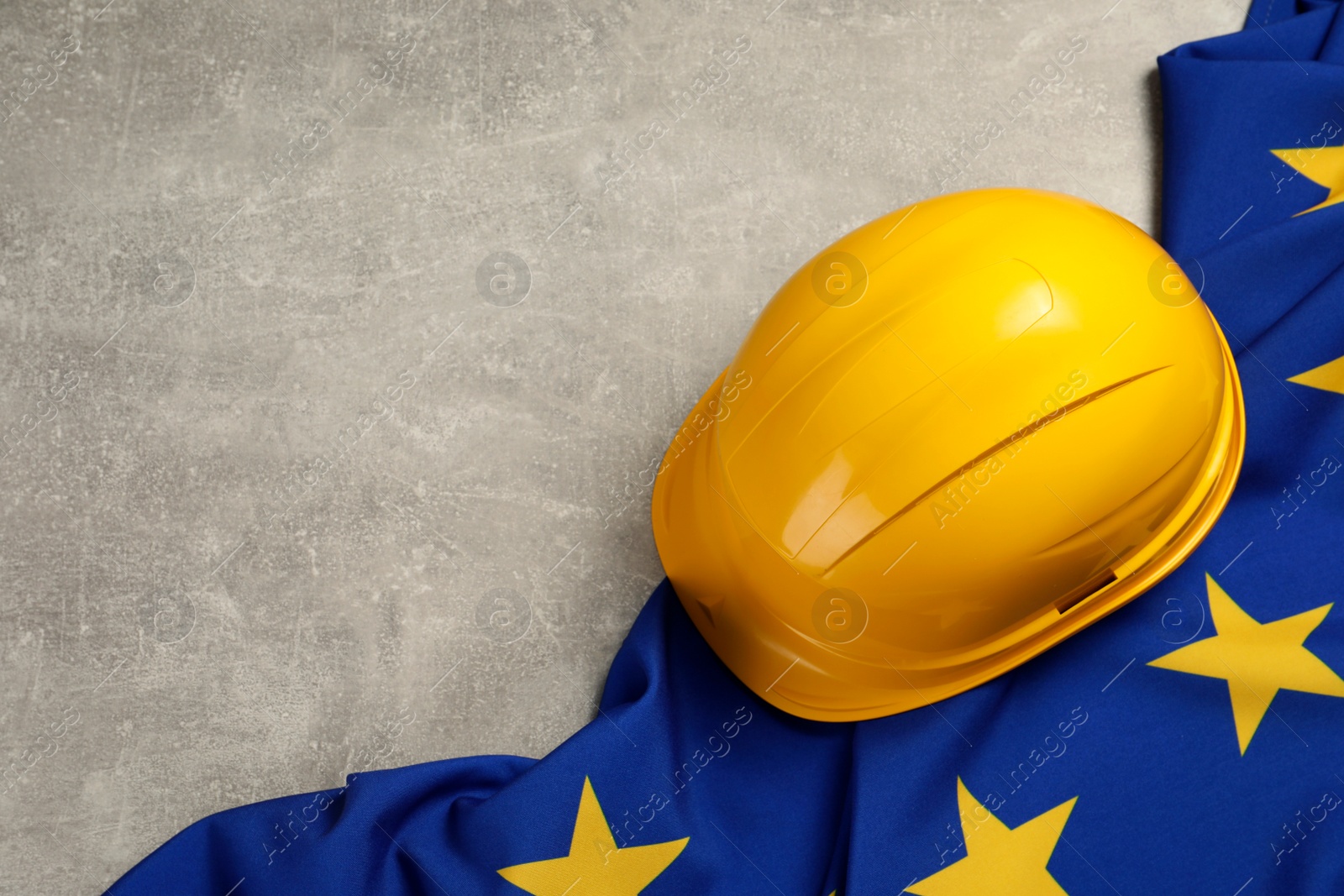 Photo of Yellow hard hat and flag of European Union on light grey table, above view. Space for text