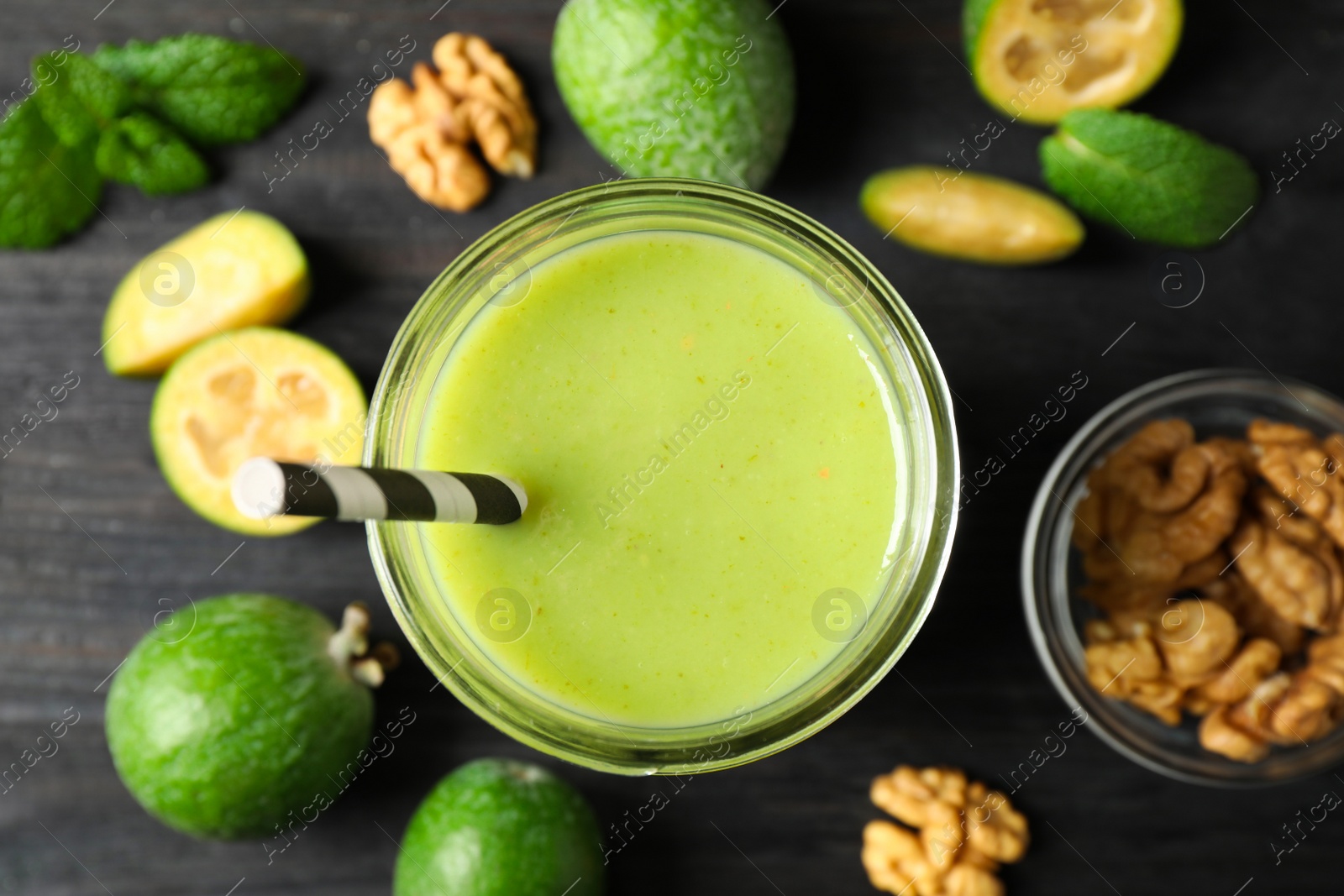 Photo of Fresh feijoa smoothie in glass on black wooden table, flat lay