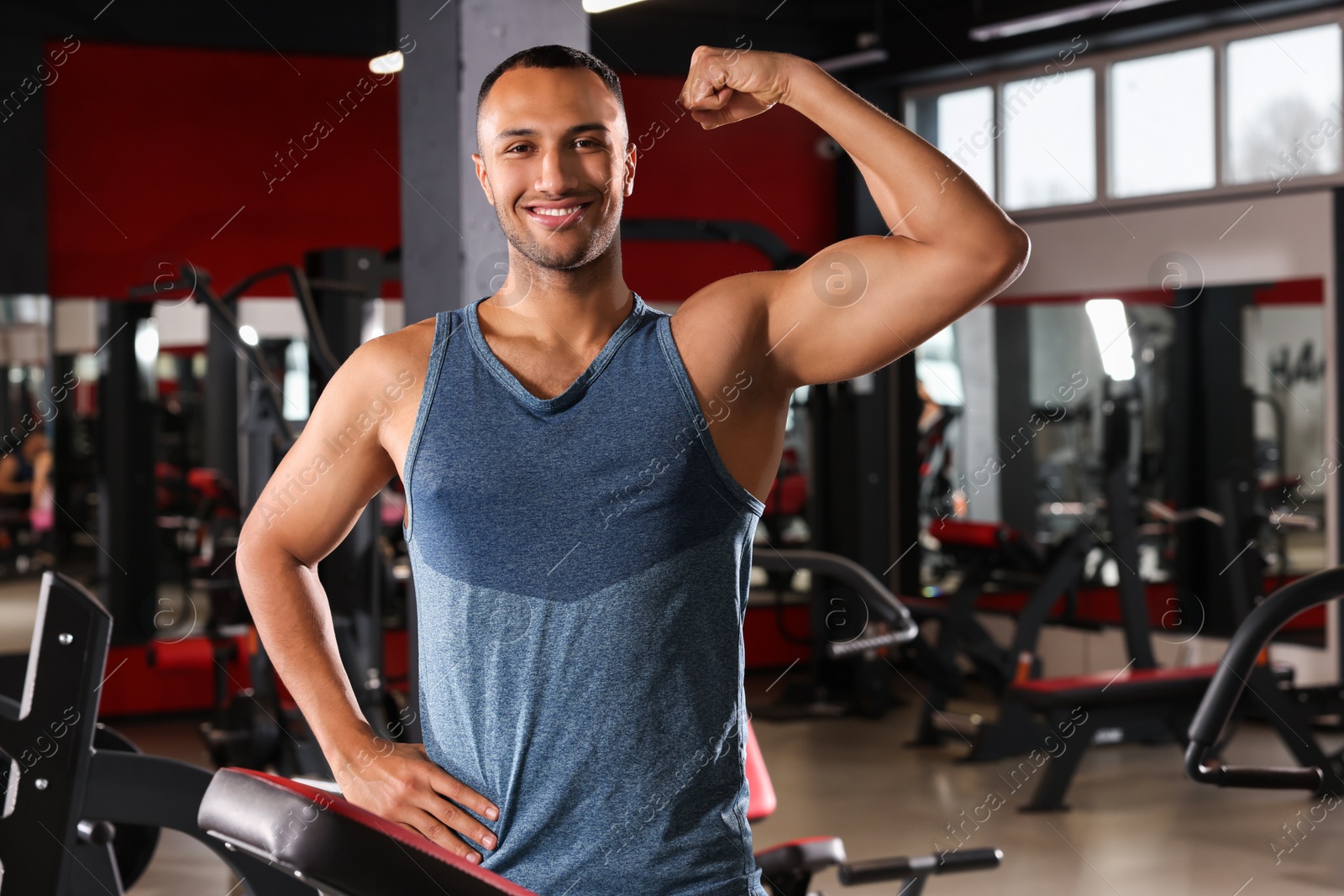 Photo of Happy trainer showing bicep in modern gym, space for text