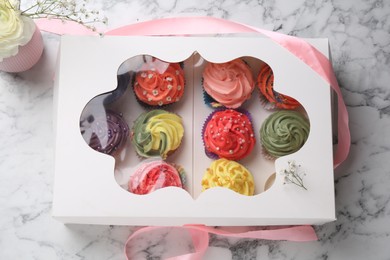 Photo of Different colorful cupcakes in box on white marble table, top view