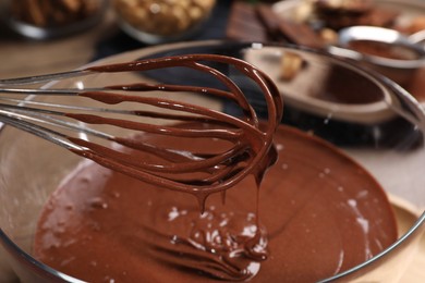 Photo of Chocolate cream flowing from whisk into bowl on table, closeup