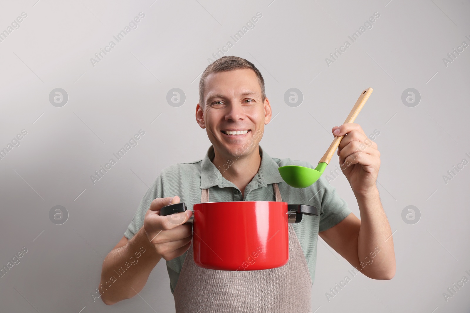 Photo of Happy man with cooking pot and ladle on light grey background