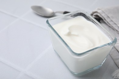 Photo of Delicious natural yogurt in glass bowl and spoon on white tiled table, closeup. Space for text