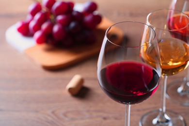 Glasses with different wines and appetizers on wooden table, closeup. Space for text