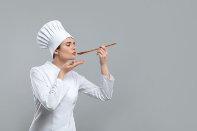 Photo of Happy female chef tasting something on light grey background. Space for text