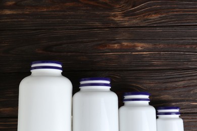 White medical bottles and pills on wooden table, flat lay. Space for text