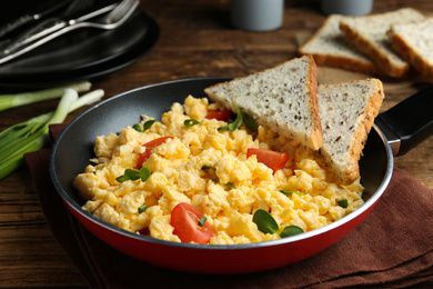 Photo of Tasty scrambled eggs with sprouts, cherry tomato and bread in frying pan on table
