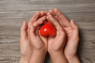 Woman and child holding heart on wooden background, top view. Donation concept