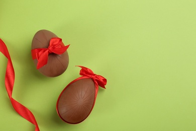 Photo of Sweet chocolate eggs with red bows and ribbon on light green background, flat lay. Space for text