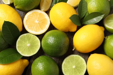 Photo of Fresh ripe lemons, limes and green leaves as background, top view