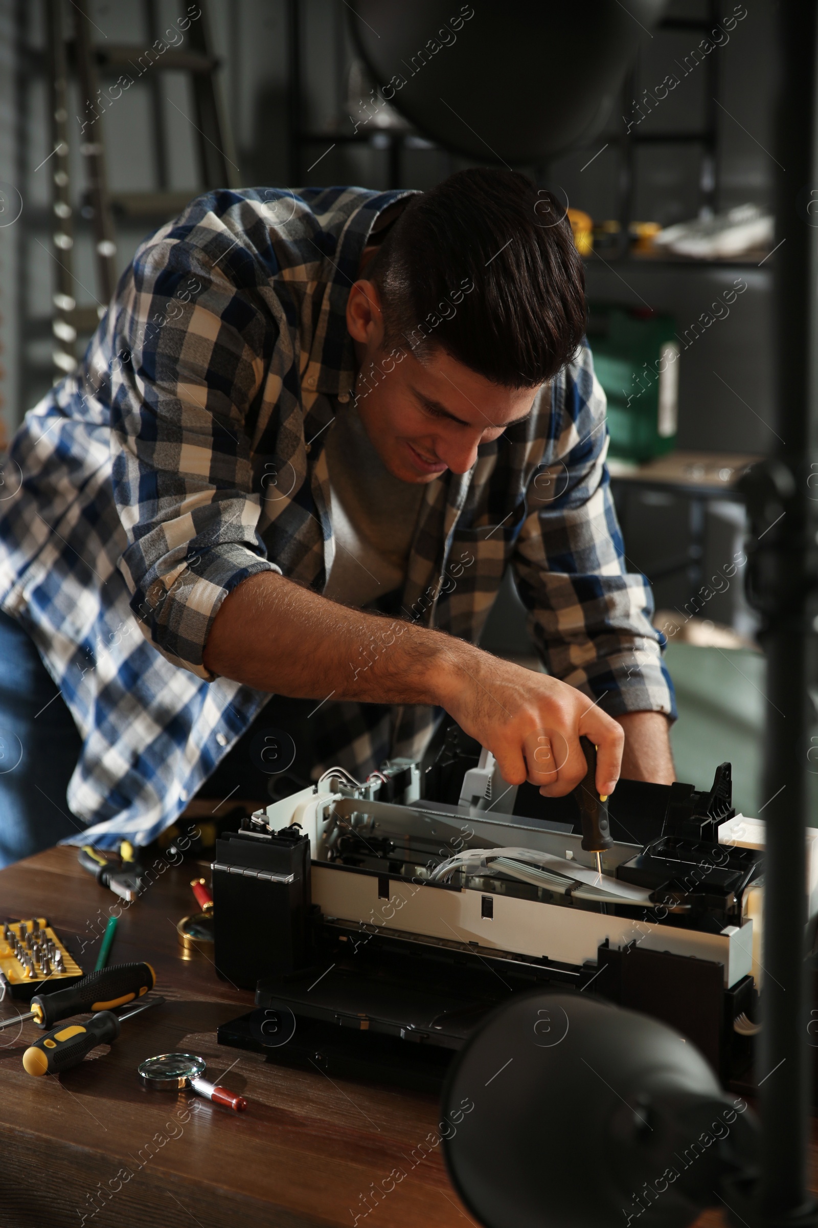 Photo of Repairman with screwdriver fixing modern printer in office