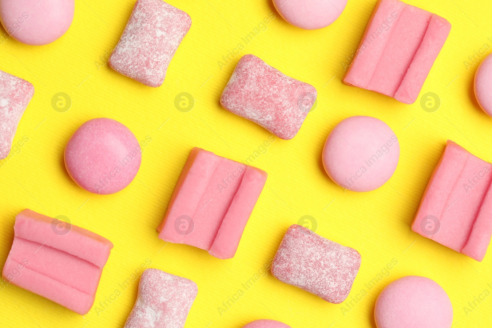 Photo of Pink bubble gums on yellow background, flat lay