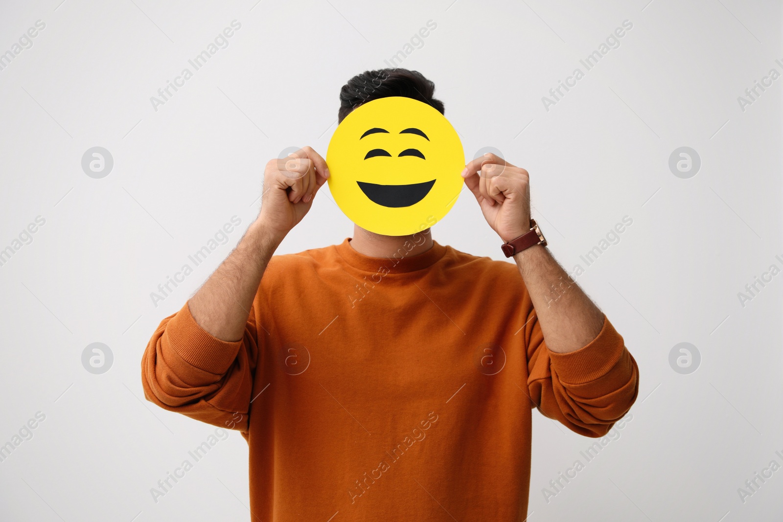 Photo of Man hiding emotions using card with drawn smiling face on white background