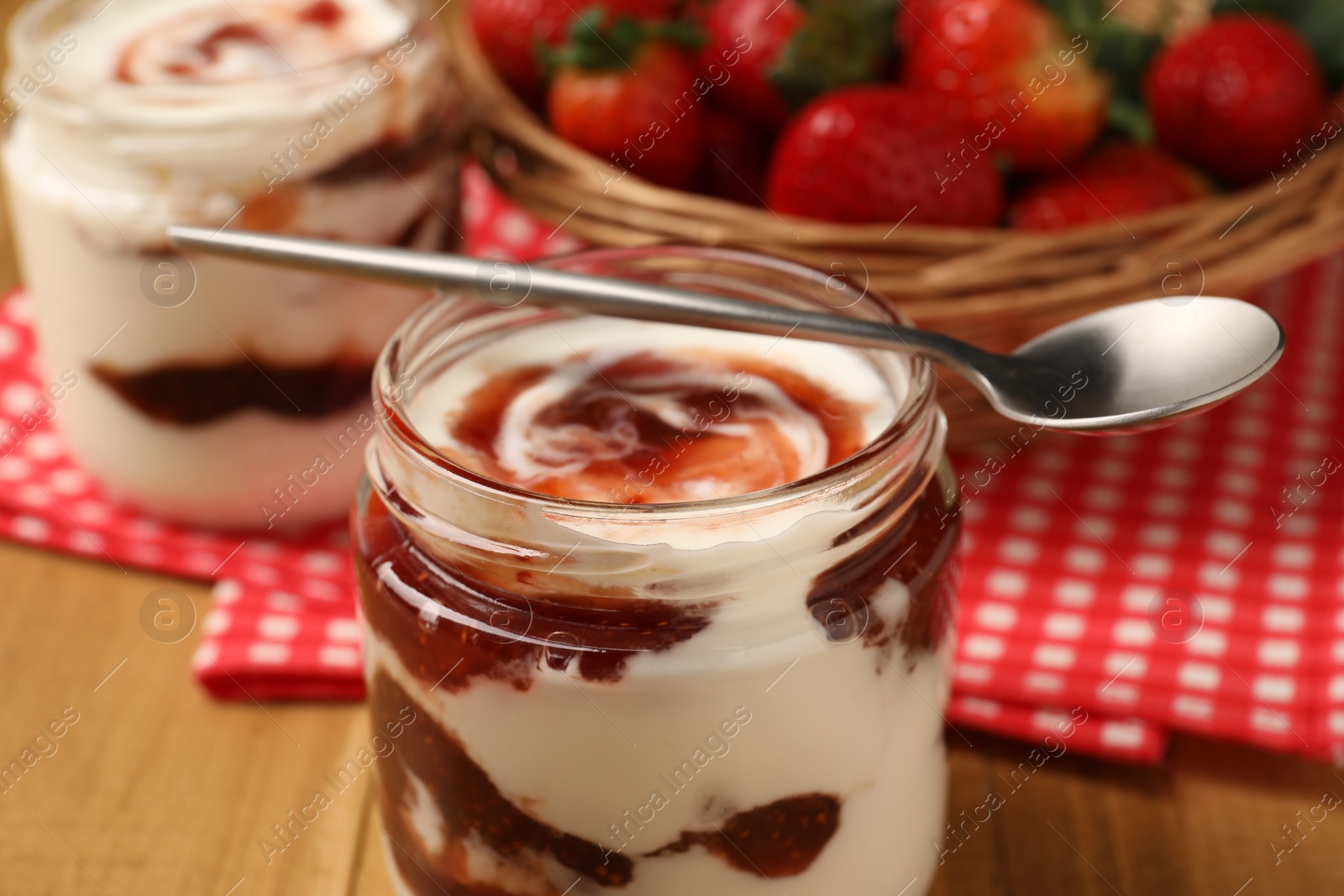 Photo of Tasty yoghurt with jam and strawberries on wooden table, closeup