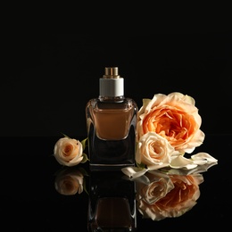 Photo of Elegant bottle of perfume and beautiful flowers on black background
