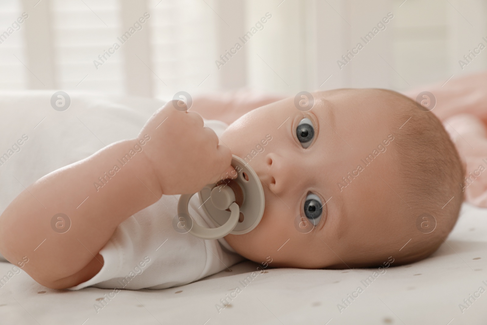Photo of Cute little baby with pacifier lying on bed at home, closeup
