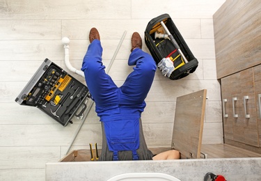 Photo of Professional plumber with set of tools working indoors, top view