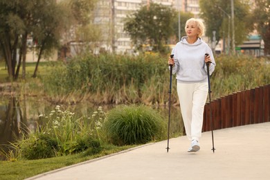 Photo of Senior woman performing Nordic walking outdoors, space for text