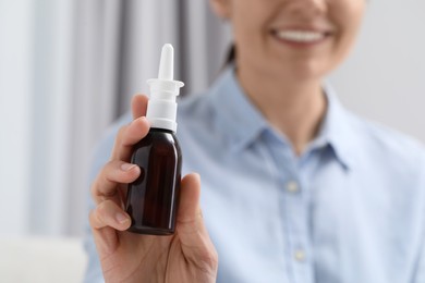 Woman holding nasal spray bottle indoors, closeup. Space for text