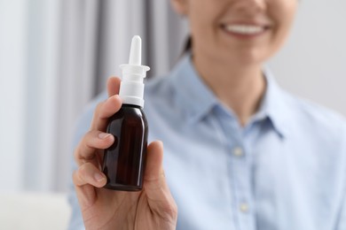 Photo of Woman holding nasal spray bottle indoors, closeup. Space for text