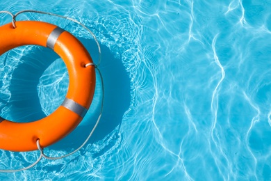 Lifebuoy floating in swimming pool on sunny day. Space for text