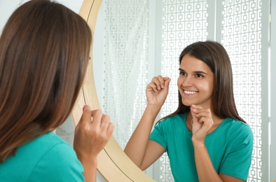 Photo of Young woman flossing her teeth near mirror at home. Cosmetic dentistry