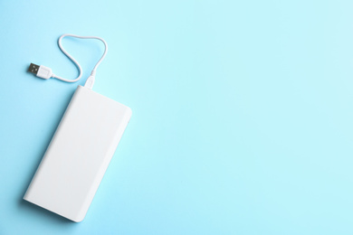 Photo of Modern portable charger with cable on light blue background, top view. Space for text