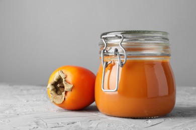 Photo of Delicious persimmon jam and fresh fruit on grey table