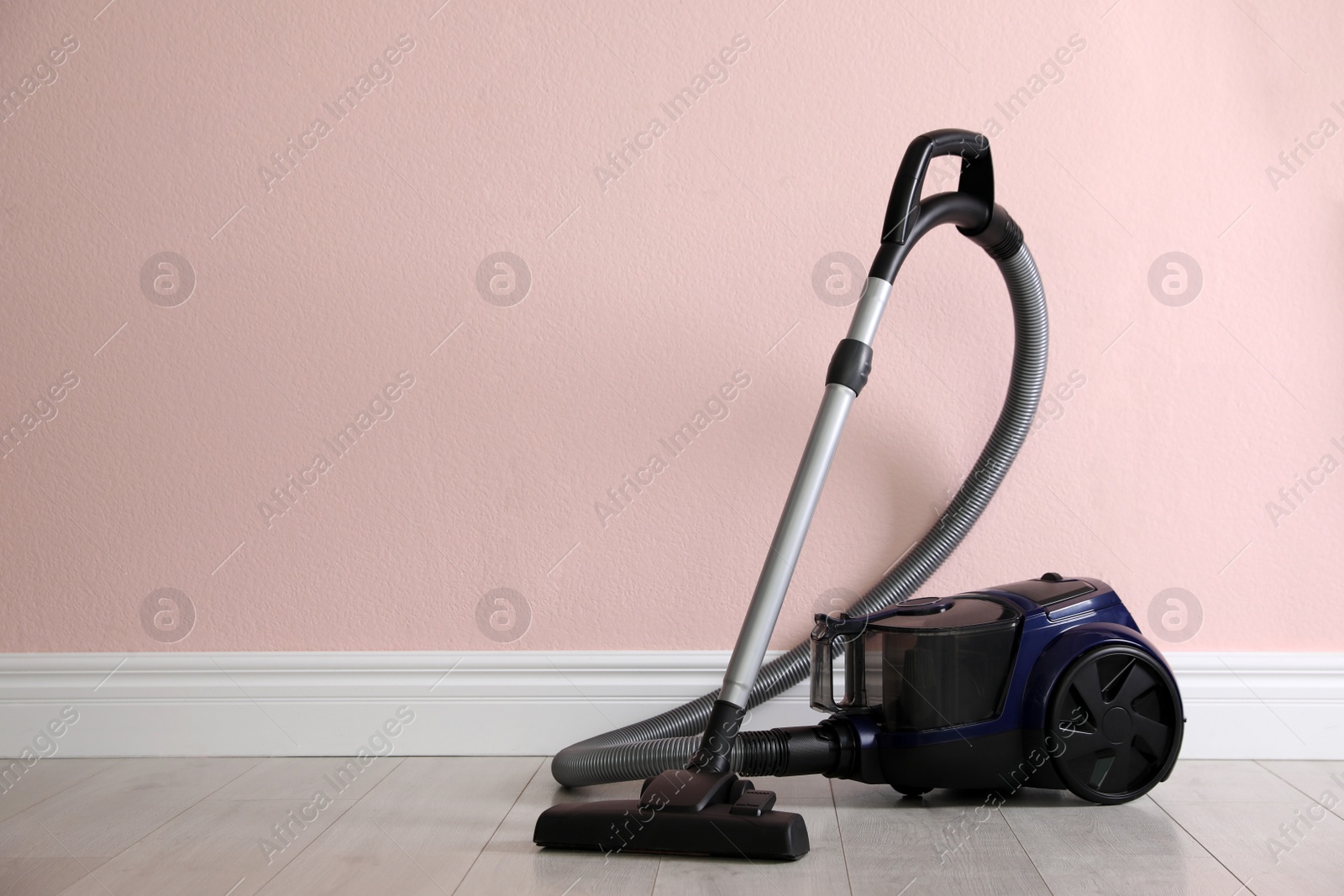 Photo of Modern vacuum cleaner near pink wall indoors, space for text