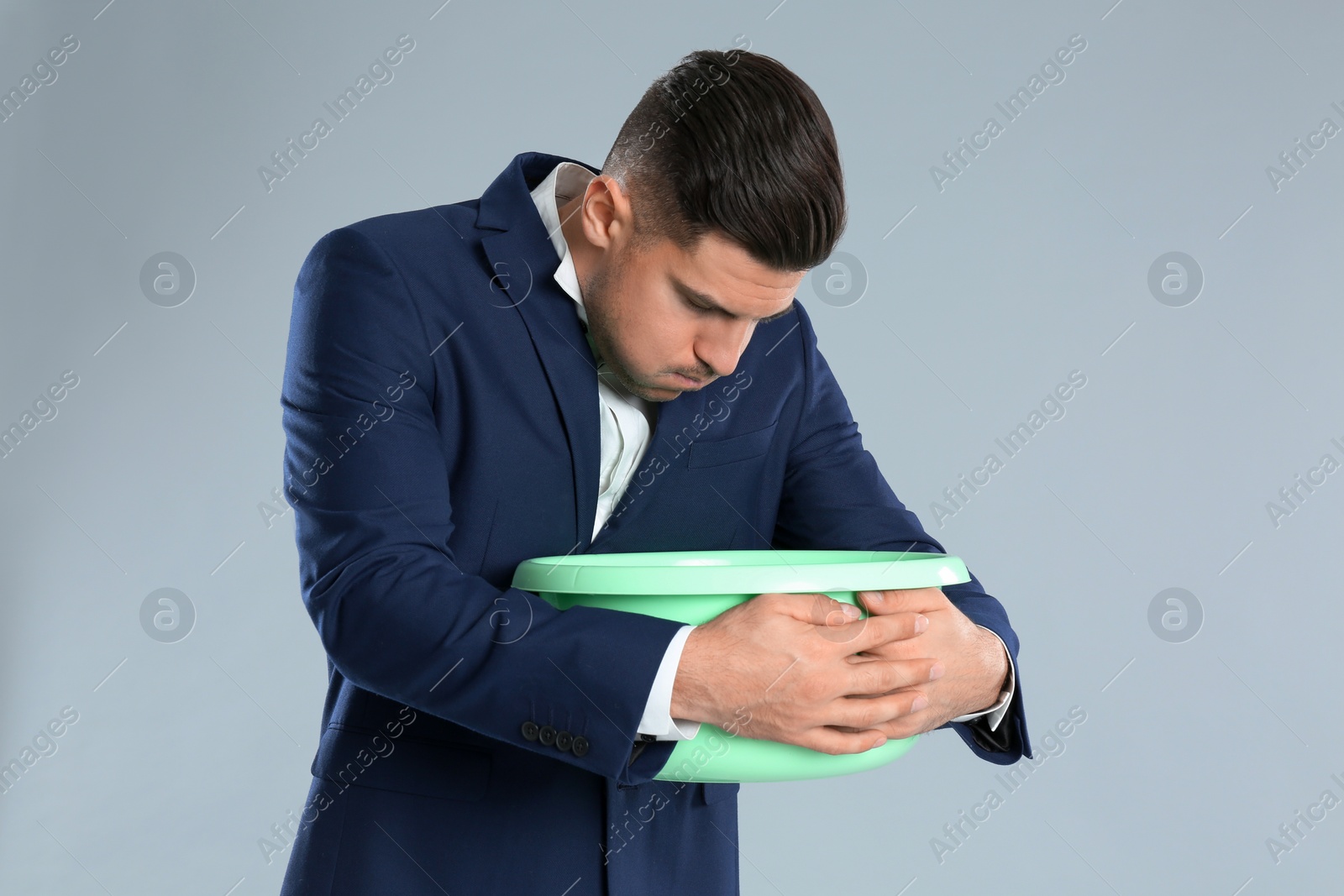 Photo of Man with basin suffering from nausea on grey background. Food poisoning