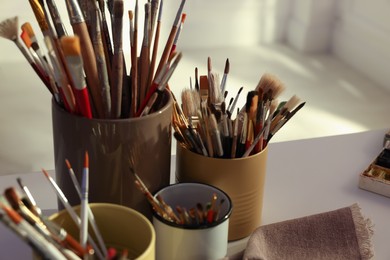 Photo of Different paintbrushes on white table indoors, closeup. Artist's workplace