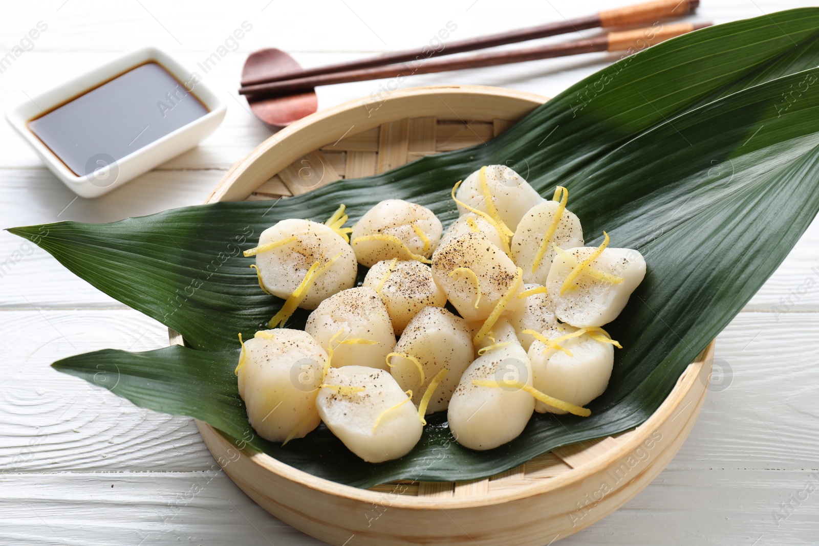 Photo of Raw scallops with milled pepper and lemon zest on white wooden table, closeup