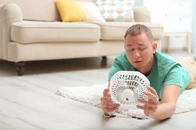Photo of Young man suffering from heat in front of small fan at home