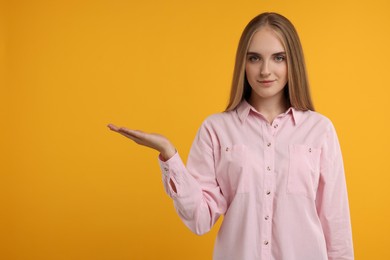 Photo of Special promotion. Young woman showing something on orange background, space for text