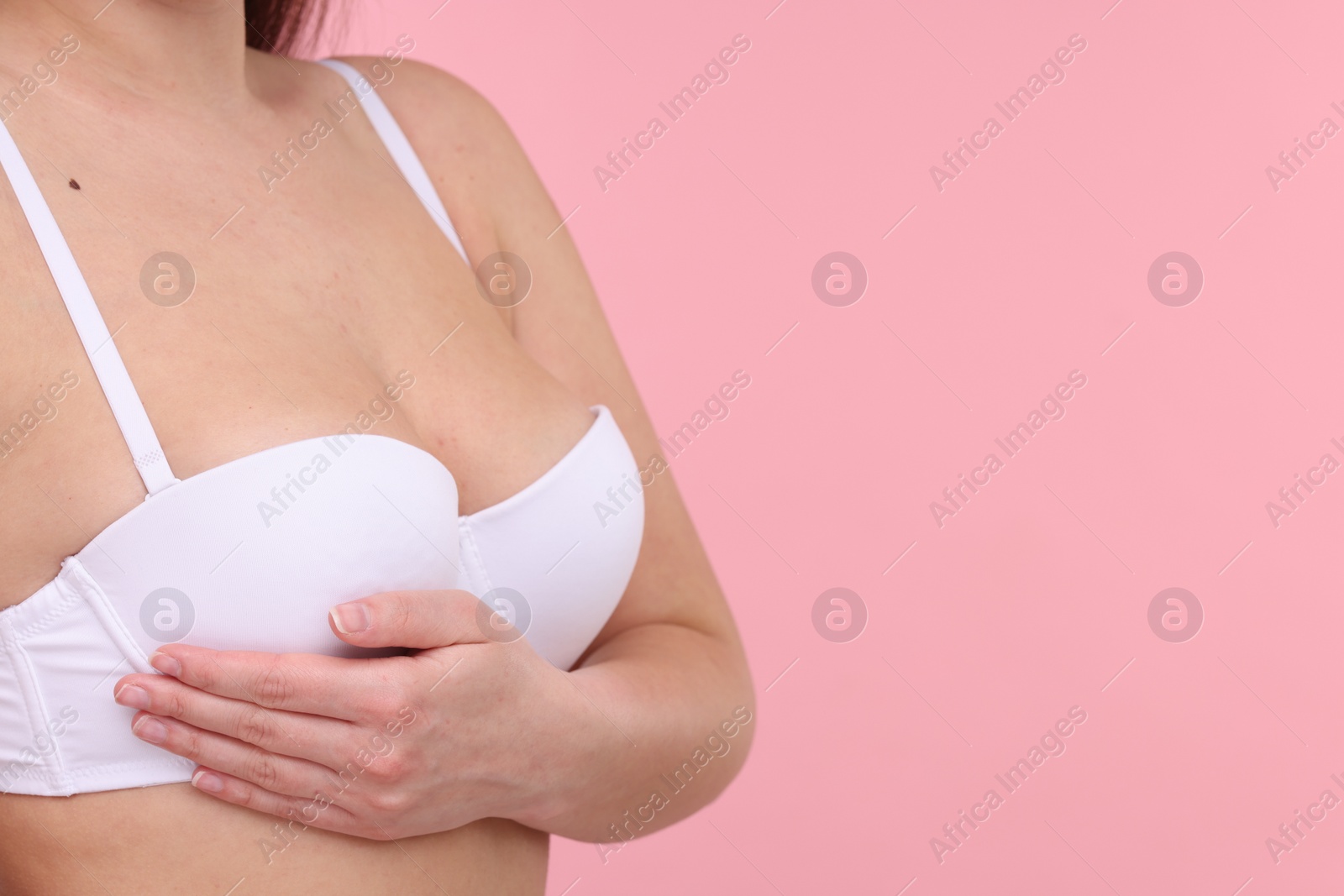 Photo of Mammology. Woman in bra doing breast self-examination on pink background, closeup and space for text